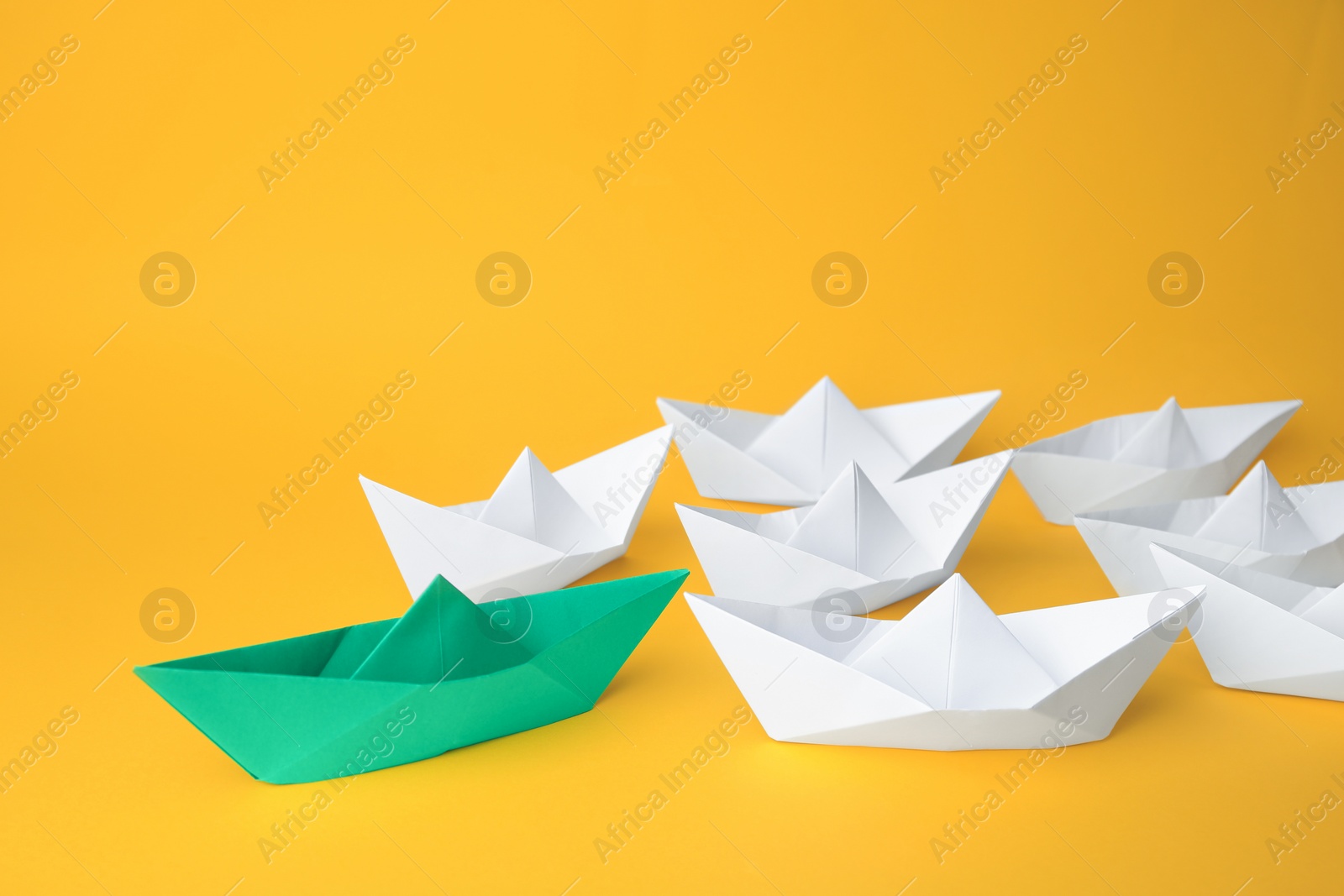 Photo of Group of paper boats following green one on yellow background. Leadership concept