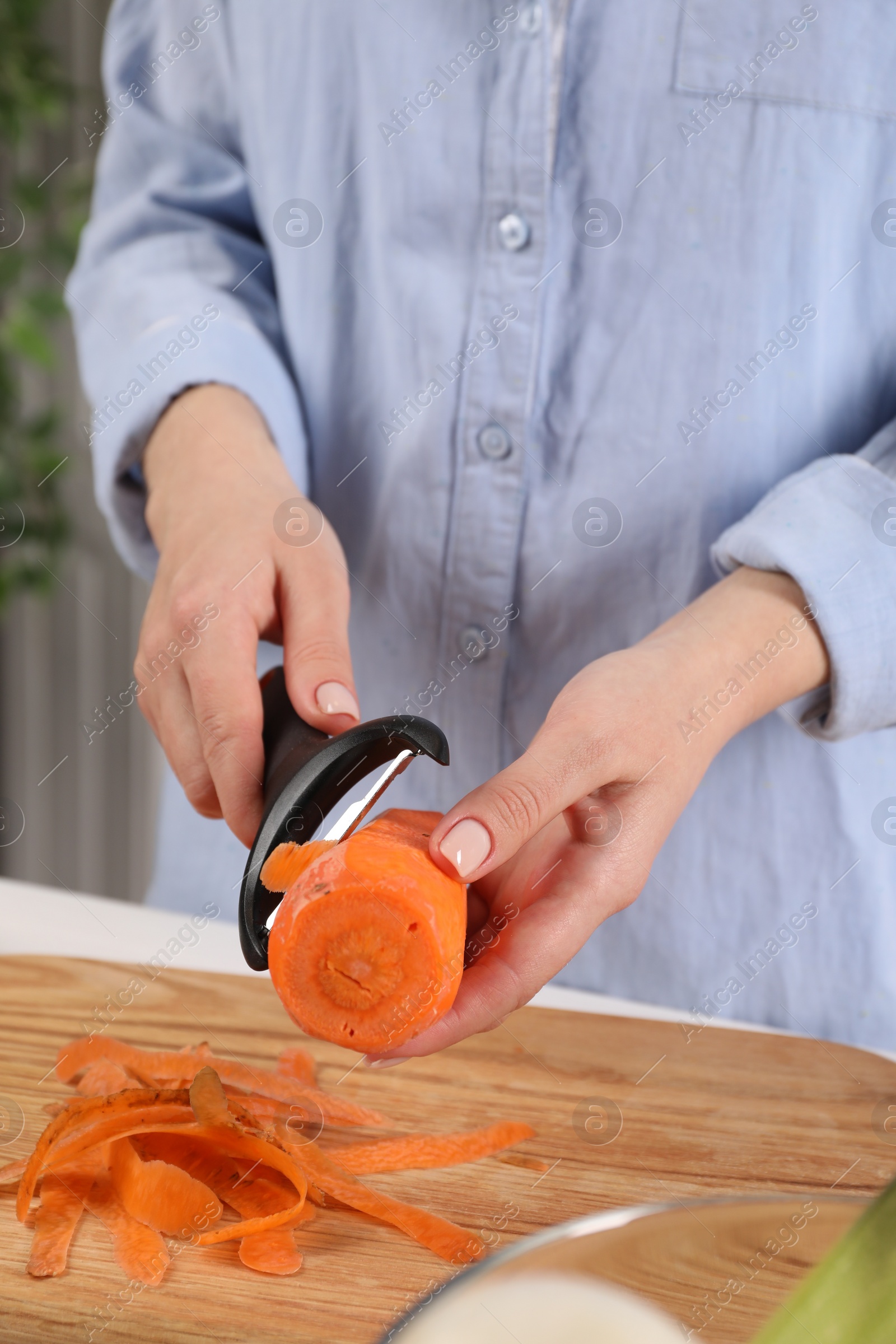 Photo of Woman peeling fresh carrot at table indoors, closeup