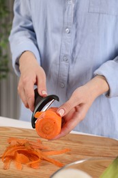 Photo of Woman peeling fresh carrot at table indoors, closeup