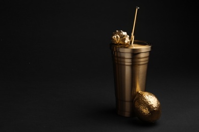 Photo of Gold cup with seashell and lemon on black background. Space for text