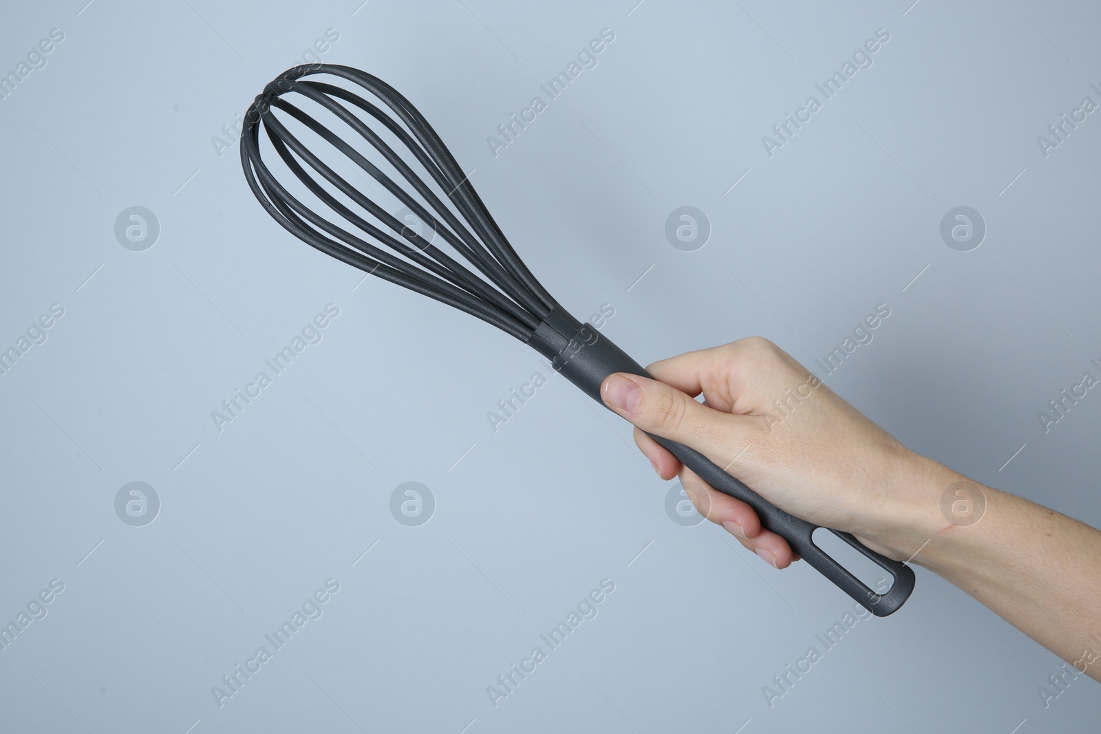 Photo of Woman holding plastic whisk on light grey background, closeup