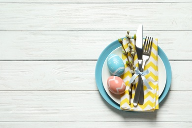 Festive Easter table setting with painted eggs on wooden background, top view. Space for text