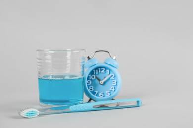 Photo of Mouthwash, toothbrush and alarm clock on light grey background, space for text