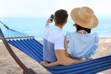 Photo of Young couple taking selfie in hammock at seaside