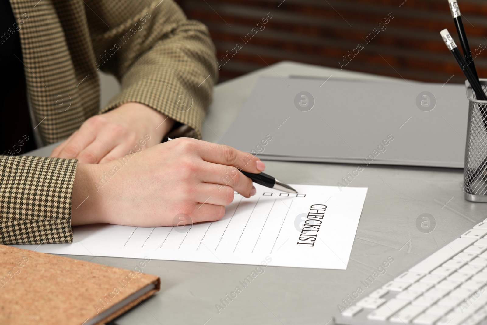 Photo of Woman filling Checklist at light grey table, closeup