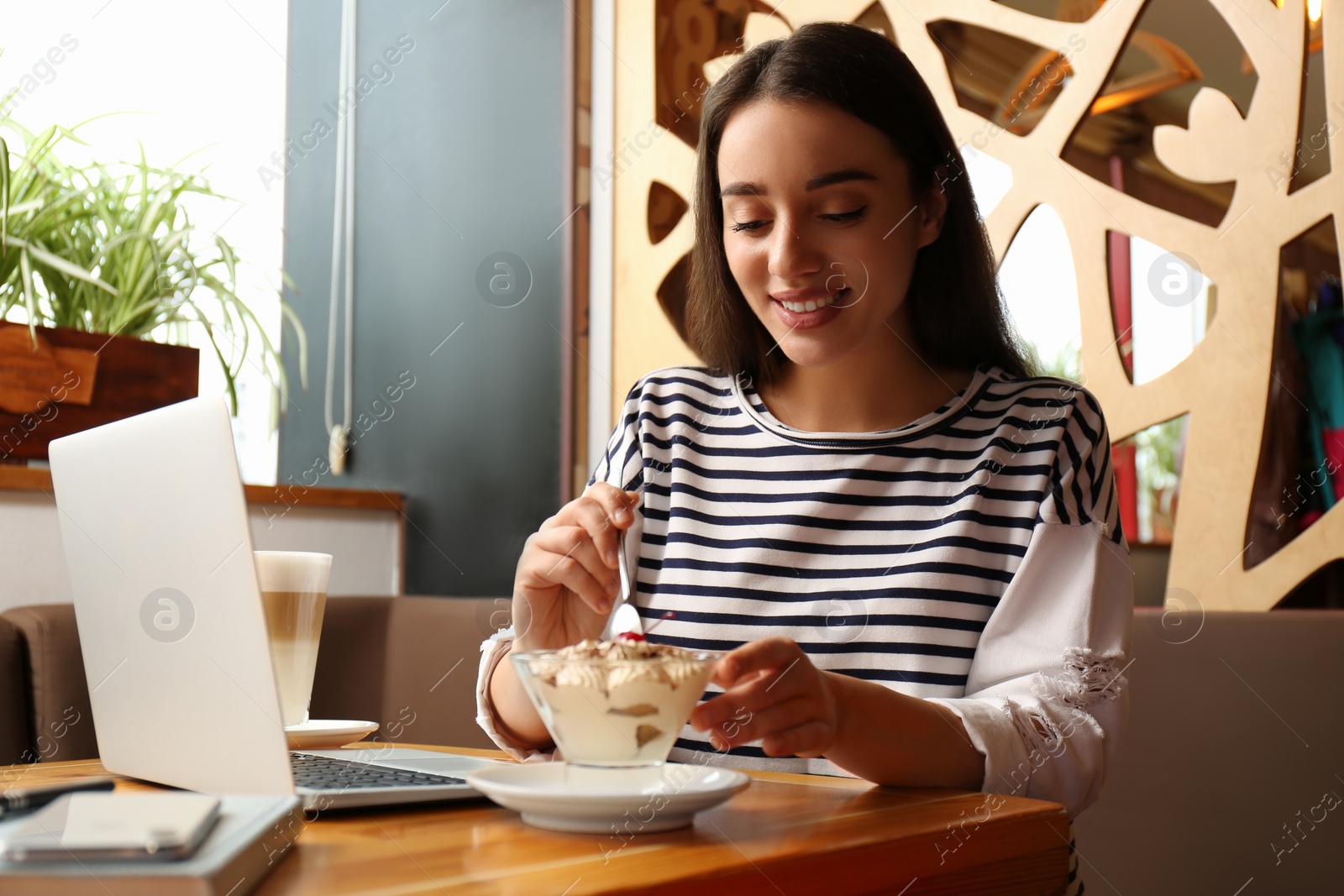 Photo of Young blogger with laptop eating dessert in cafe