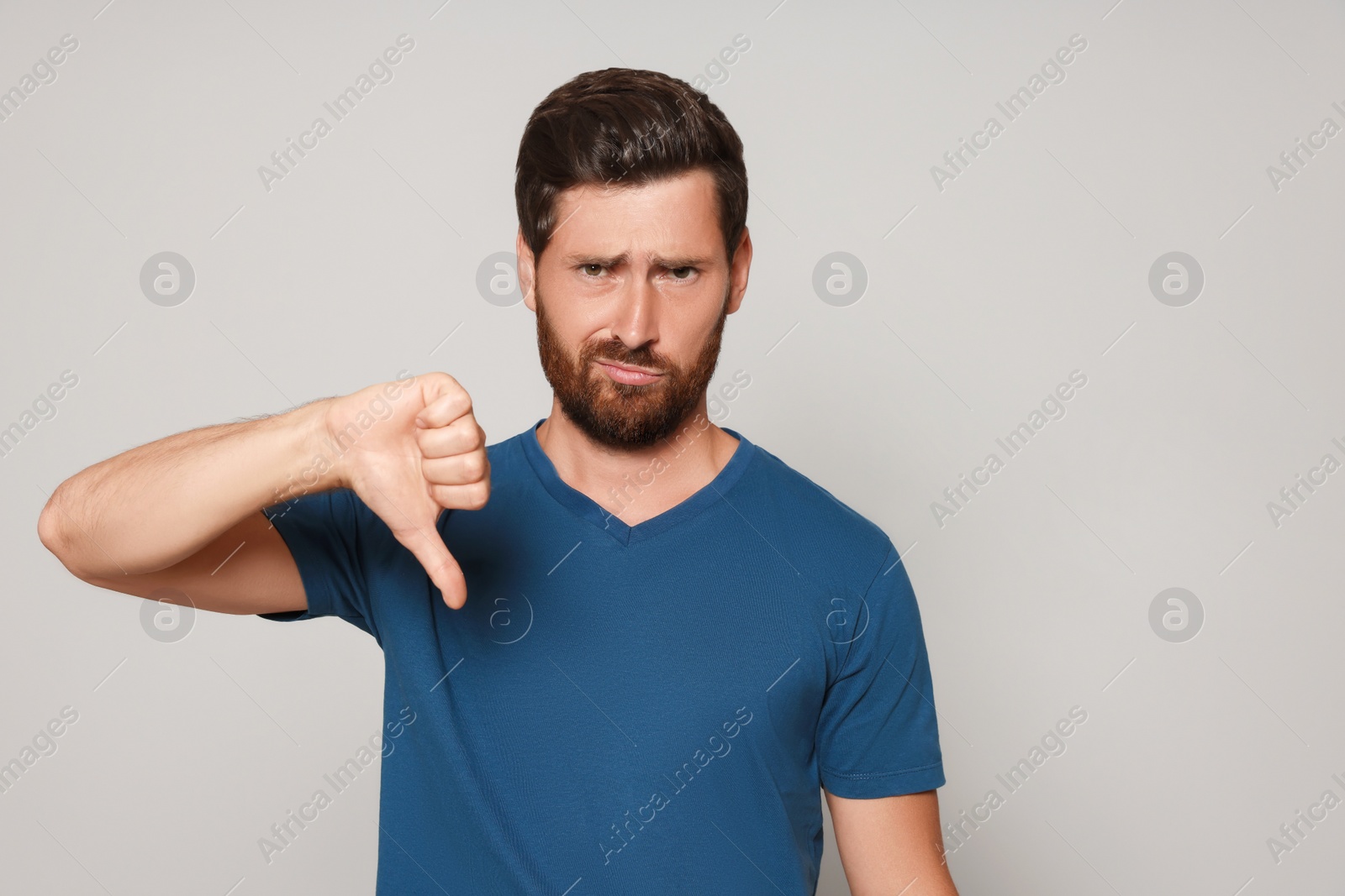 Photo of Handsome bearded man showing thumb down on light grey background. Space for text