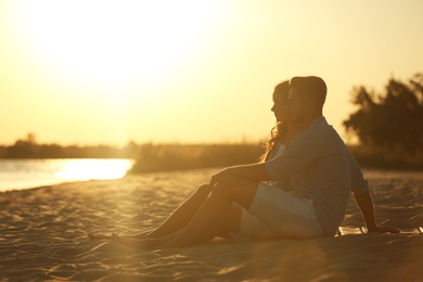 Happy young couple resting together on beach at sunset