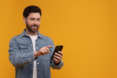 Photo of Smiling man with smartphone on orange background. Space for text