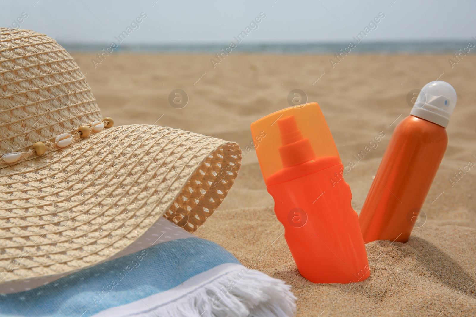 Photo of Sunscreens, hat and towel on sand, closeup. Sun protection care
