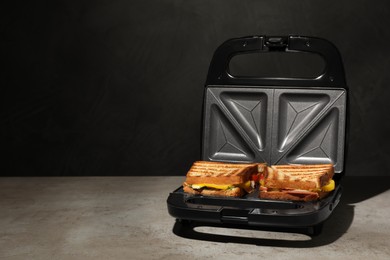 Photo of Modern grill maker with tasty sandwiches on light grey table. Space for text