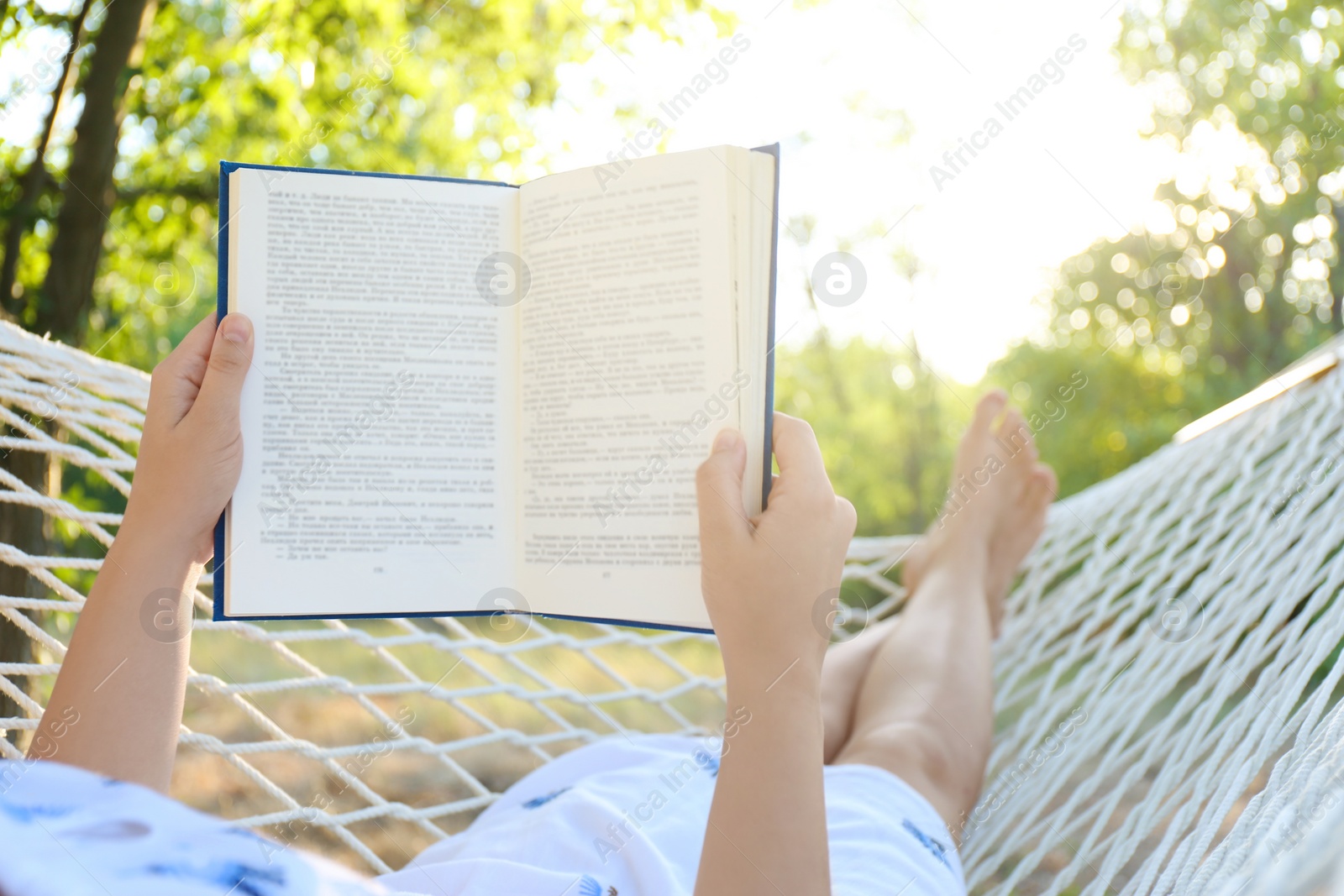 Photo of Young woman reading book in comfortable hammock at green garden, closeup