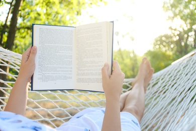Photo of Young woman reading book in comfortable hammock at green garden, closeup