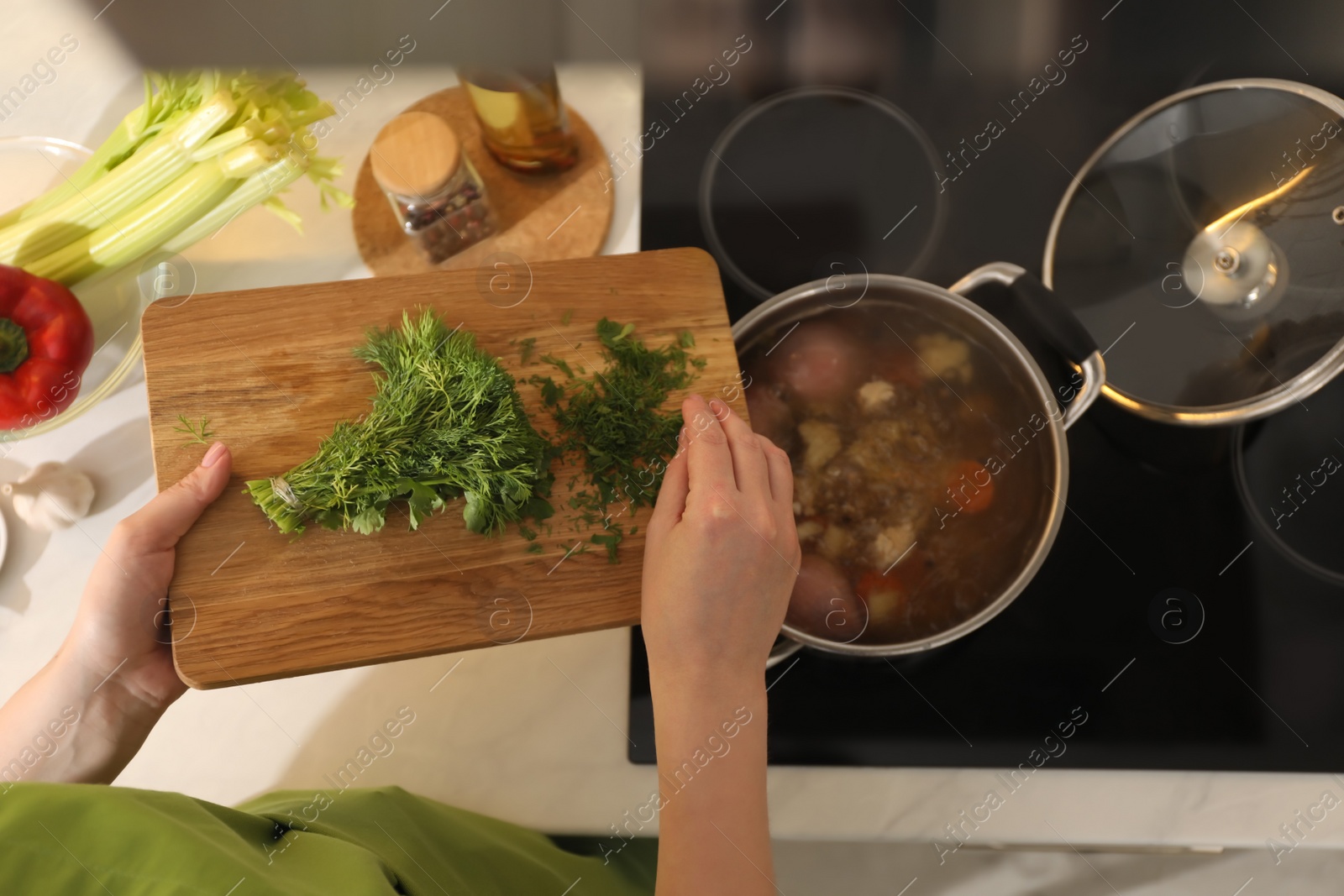 Photo of Woman putting dill into pot to make bouillon in kitchen, top view. Homemade recipe