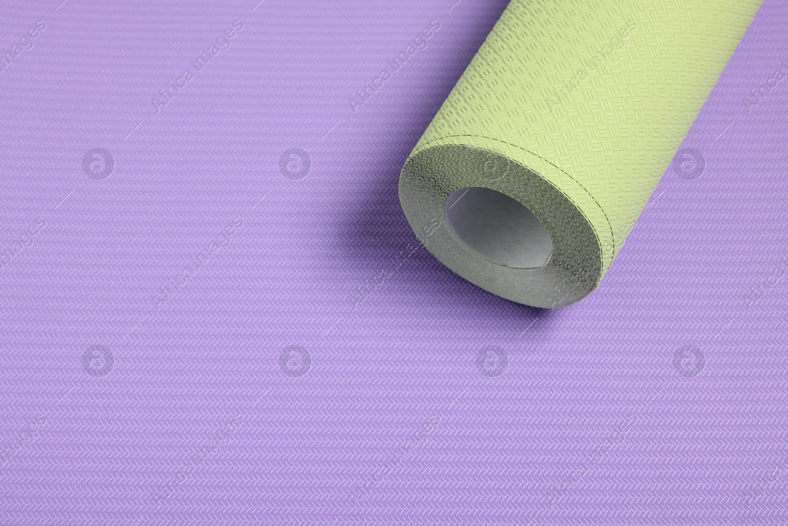 Photo of One green wallpaper roll on violet sample, above view. Space for text