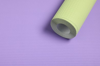 One green wallpaper roll on violet sample, above view. Space for text