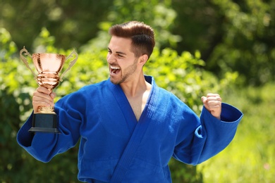 Portrait of happy young man in blue kimono with gold trophy cup outdoors