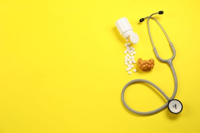 Endocrinology. Stethoscope, bottle with pills and model of thyroid gland on yellow background, flat lay. Space for text