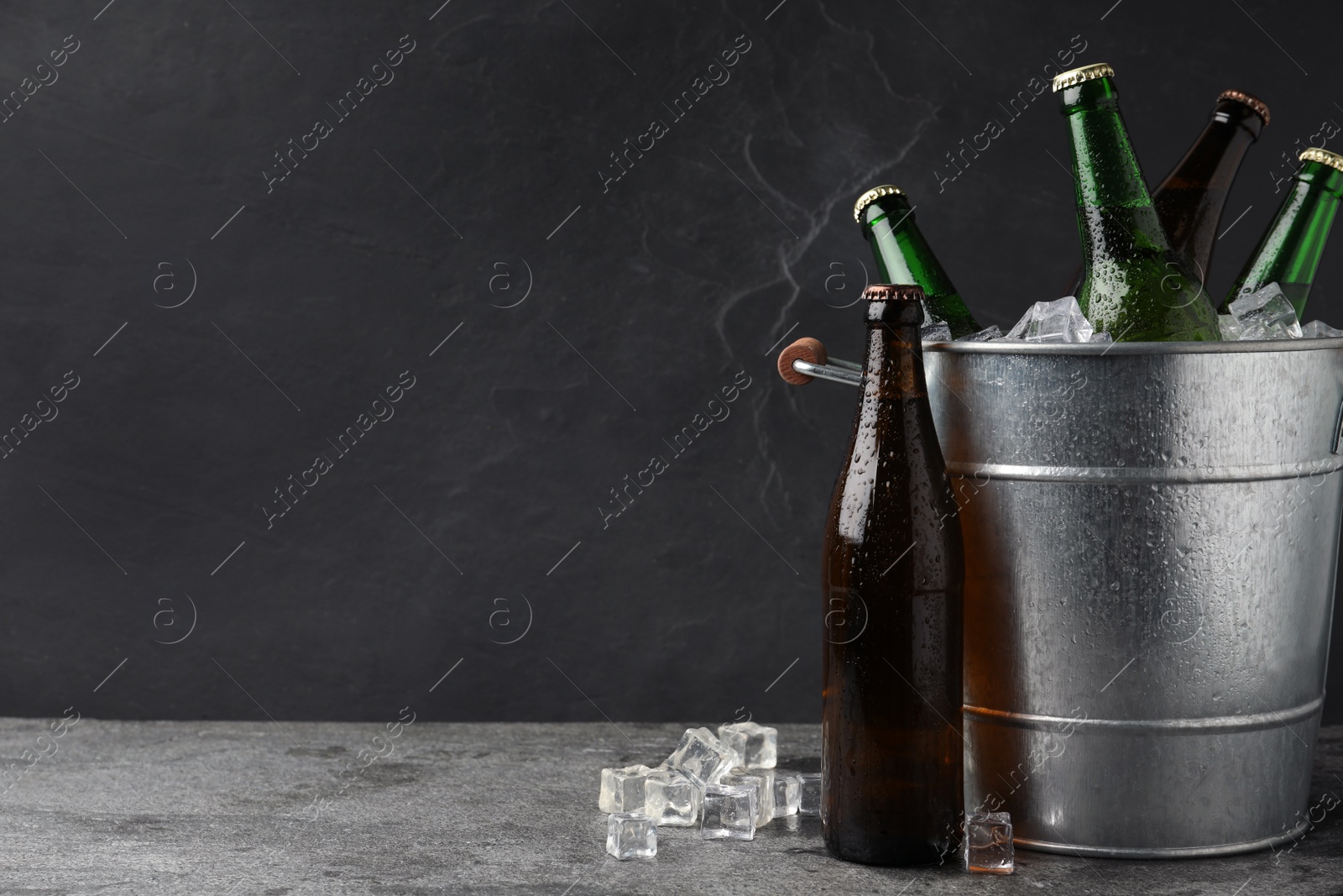 Photo of Metal bucket with beer and ice cubes on grey background. Space for text