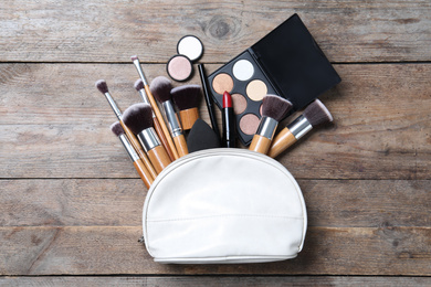 Photo of Cosmetic bag with makeup products and beauty accessories on wooden background, flat lay