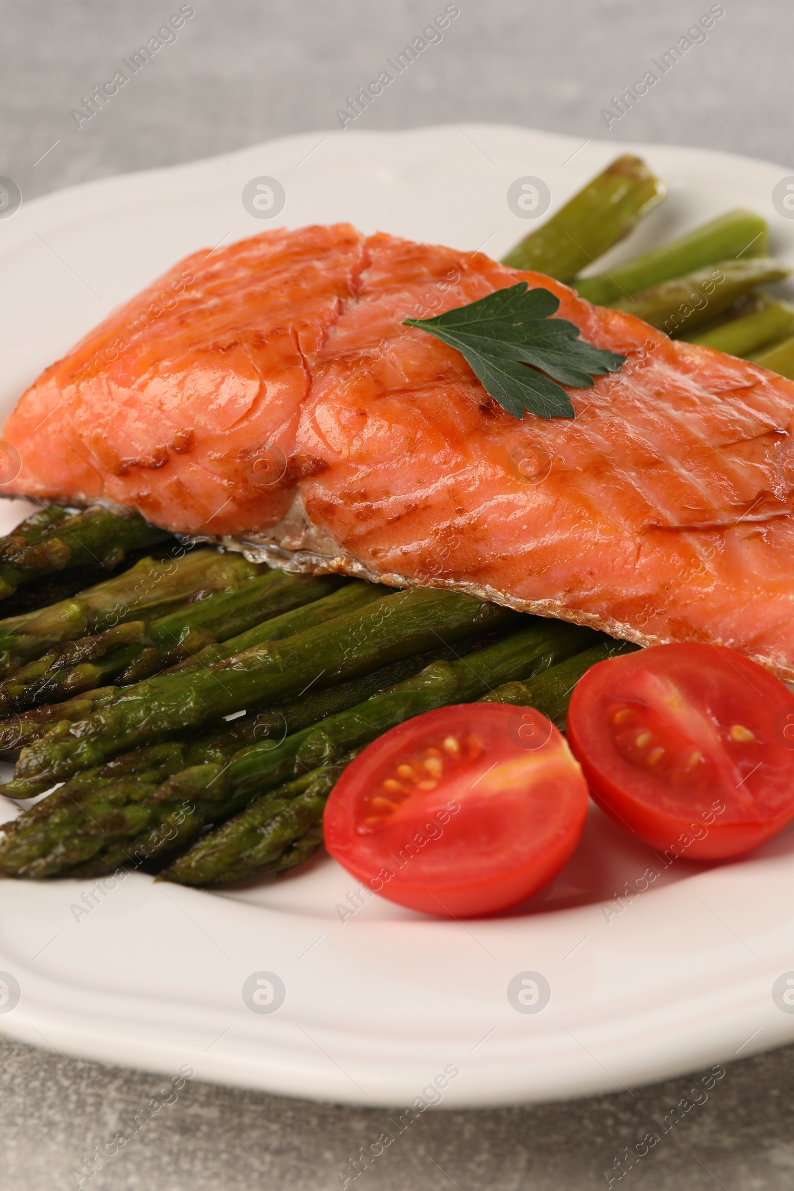 Photo of Tasty grilled salmon with tomatoes and asparagus on grey table, closeup