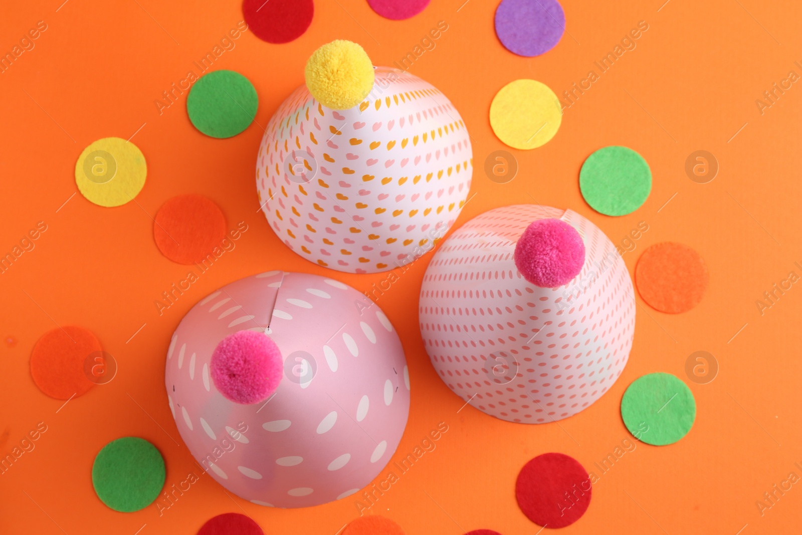 Photo of Party hats and colorful confetti on orange background, flat lay