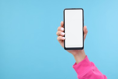 Photo of Woman holding smartphone with blank screen on light blue background, closeup. Mockup for design
