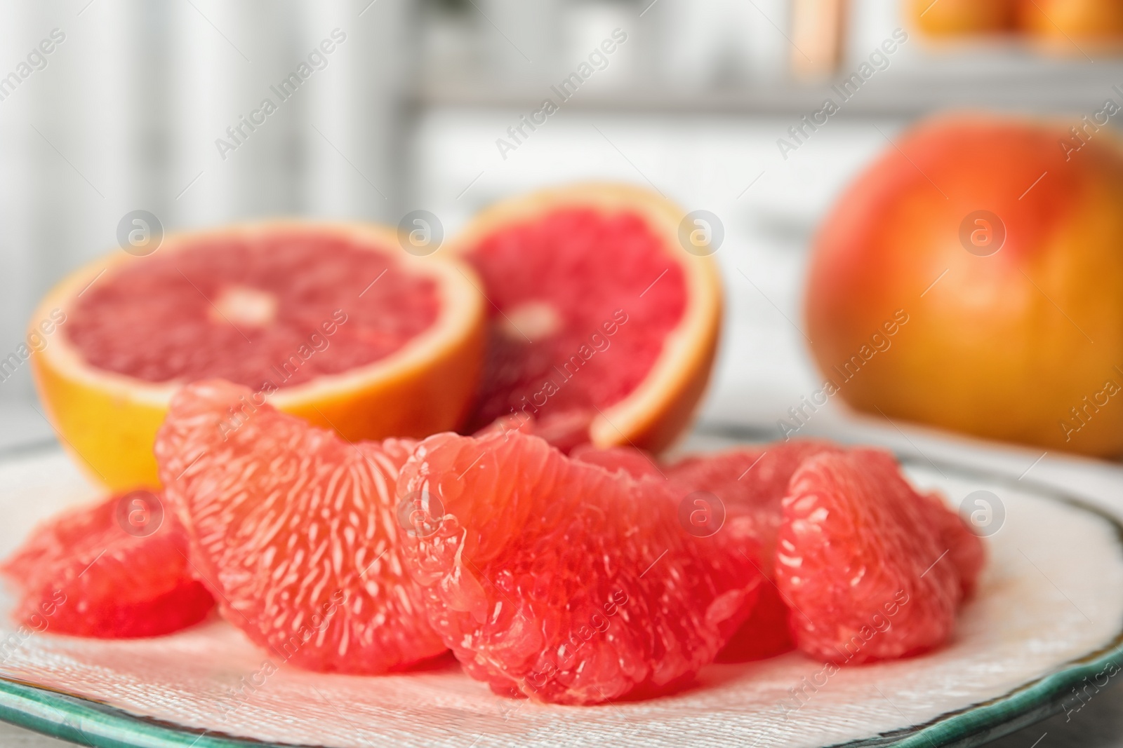 Photo of Plate with ripe grapefruits on table against blurred background