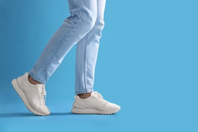 Man walking in stylish sneakers on light blue background, closeup. Space for text