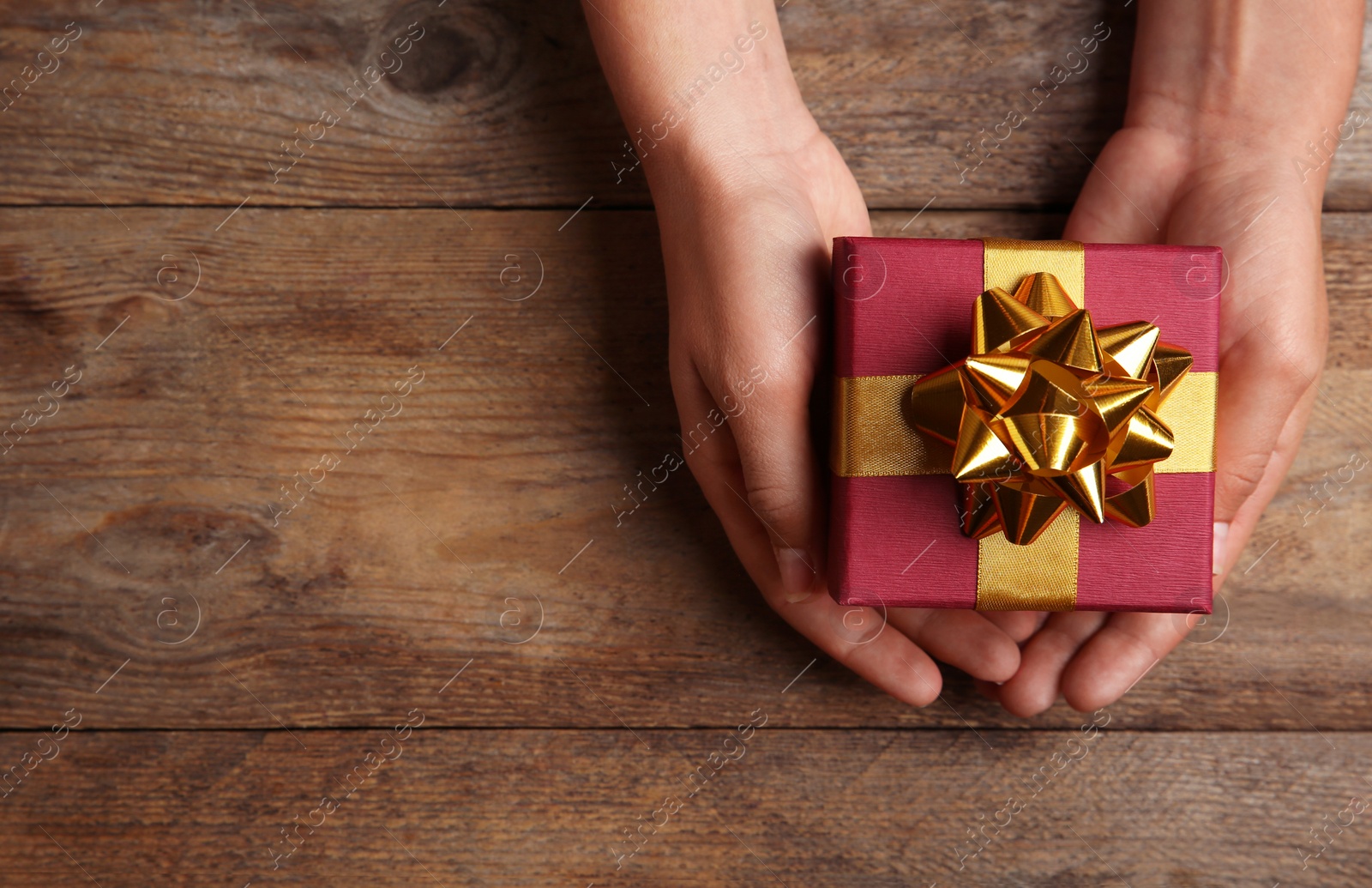 Photo of Woman holding beautiful gift box over wooden table, top view. Space for text