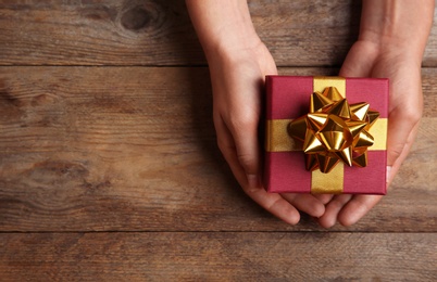 Photo of Woman holding beautiful gift box over wooden table, top view. Space for text