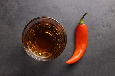Photo of Red hot chili pepper and vodka in glass on grey table, flat lay