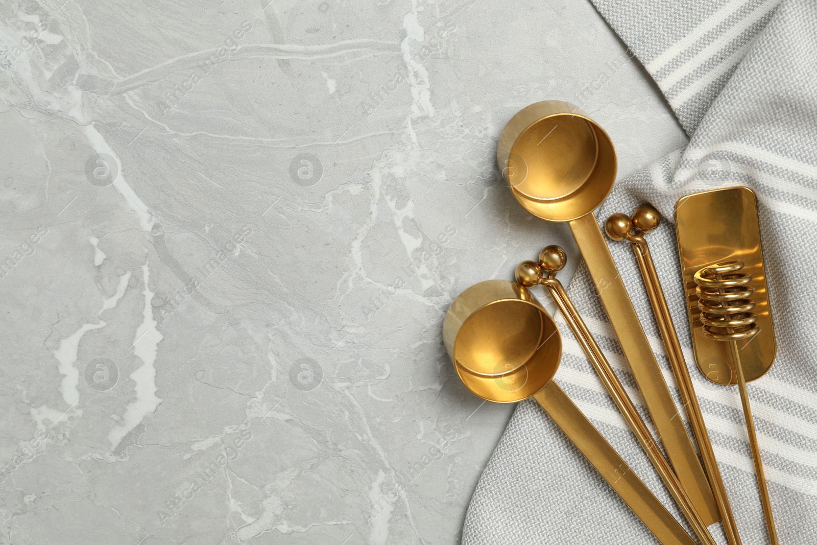 Photo of Golden cooking utensils and tablecloth on grey marble table, flat lay. Space for text