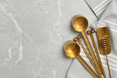 Photo of Golden cooking utensils and tablecloth on grey marble table, flat lay. Space for text