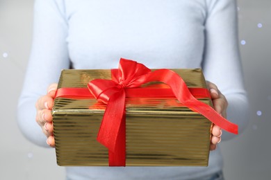 Photo of Christmas present. Woman holding gift box against grey background with blurred lights, closeup