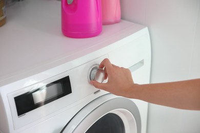 Photo of Woman turning on washing machine in bathroom, closeup. Laundry day