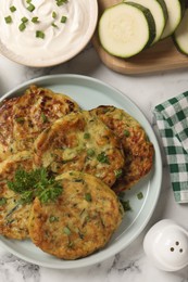 Delicious zucchini fritters served on white marble table, flat lay