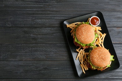 Plate with tasty burgers, french fries and sauce on wooden background, top view. Space for text