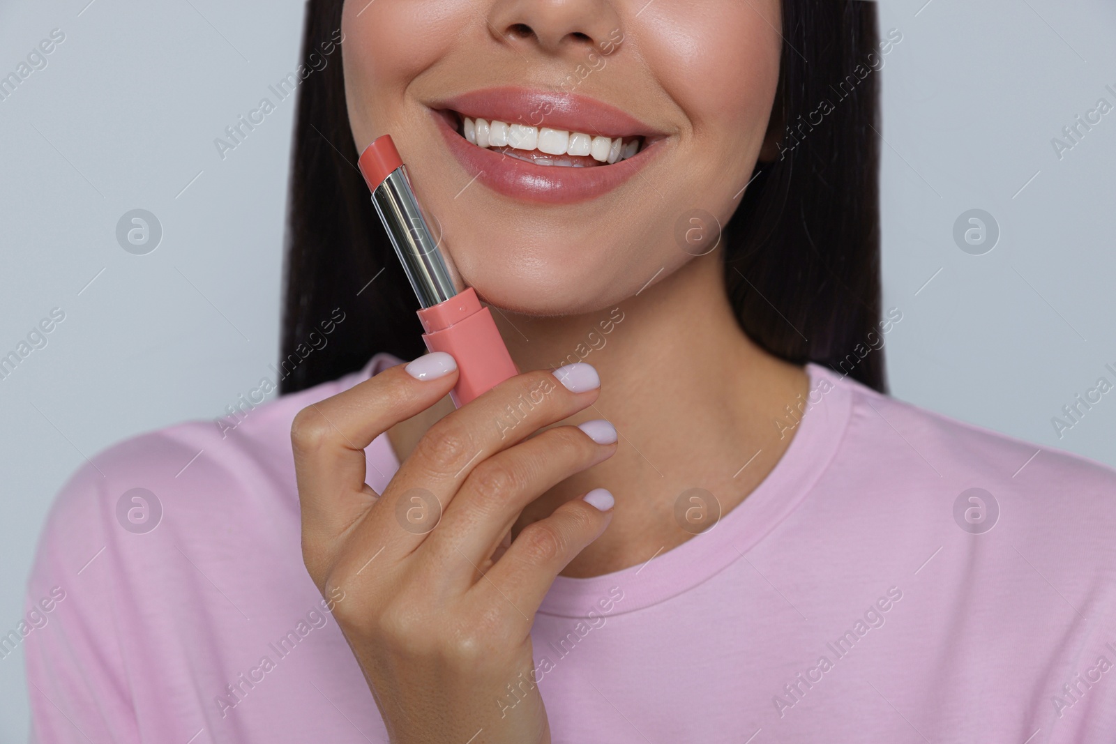 Photo of Young woman with beautiful makeup holding nude lipstick on light gray background, closeup