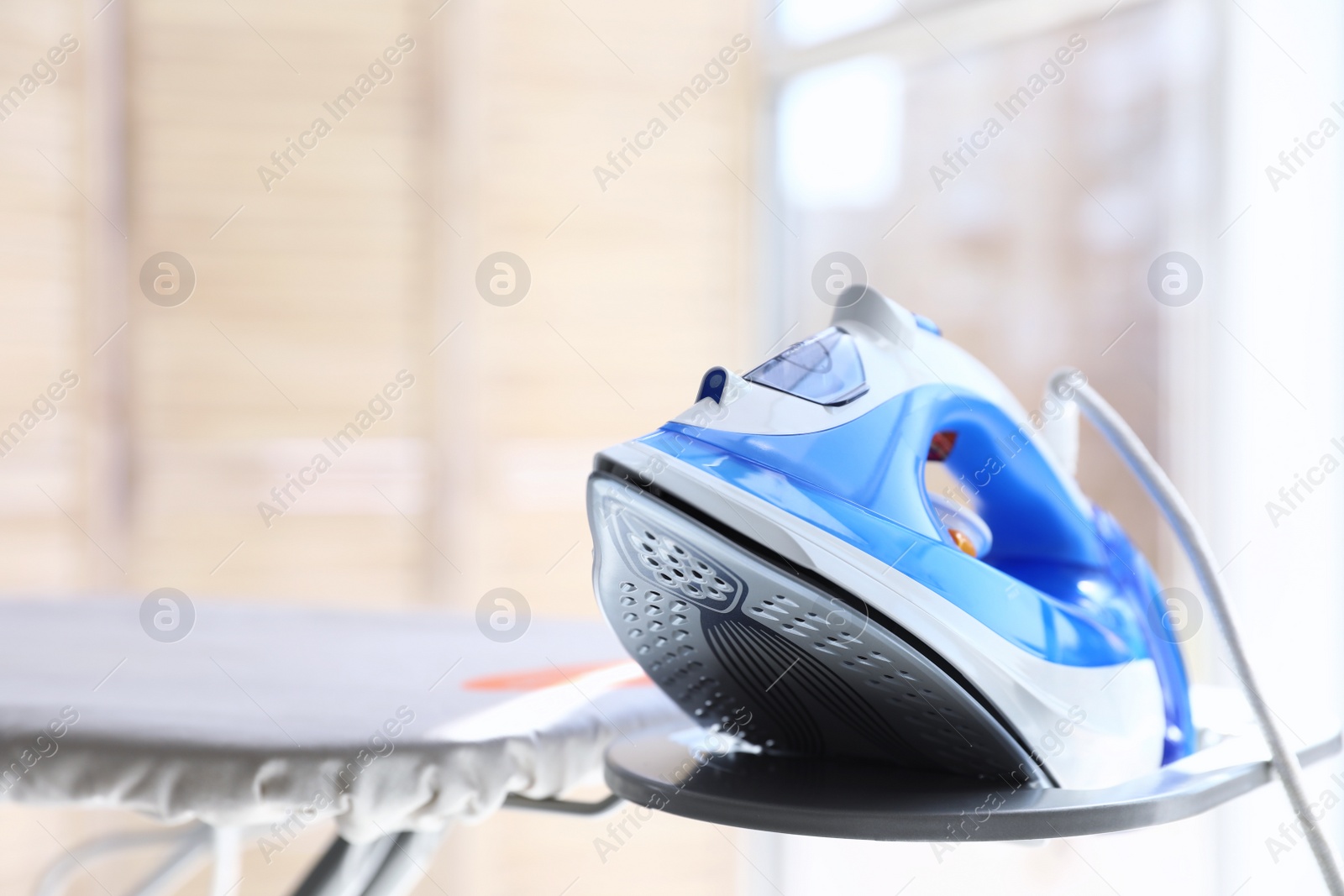 Photo of Modern electric iron on board indoors, space for text. Household appliance