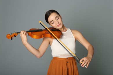 Beautiful woman playing violin on grey background