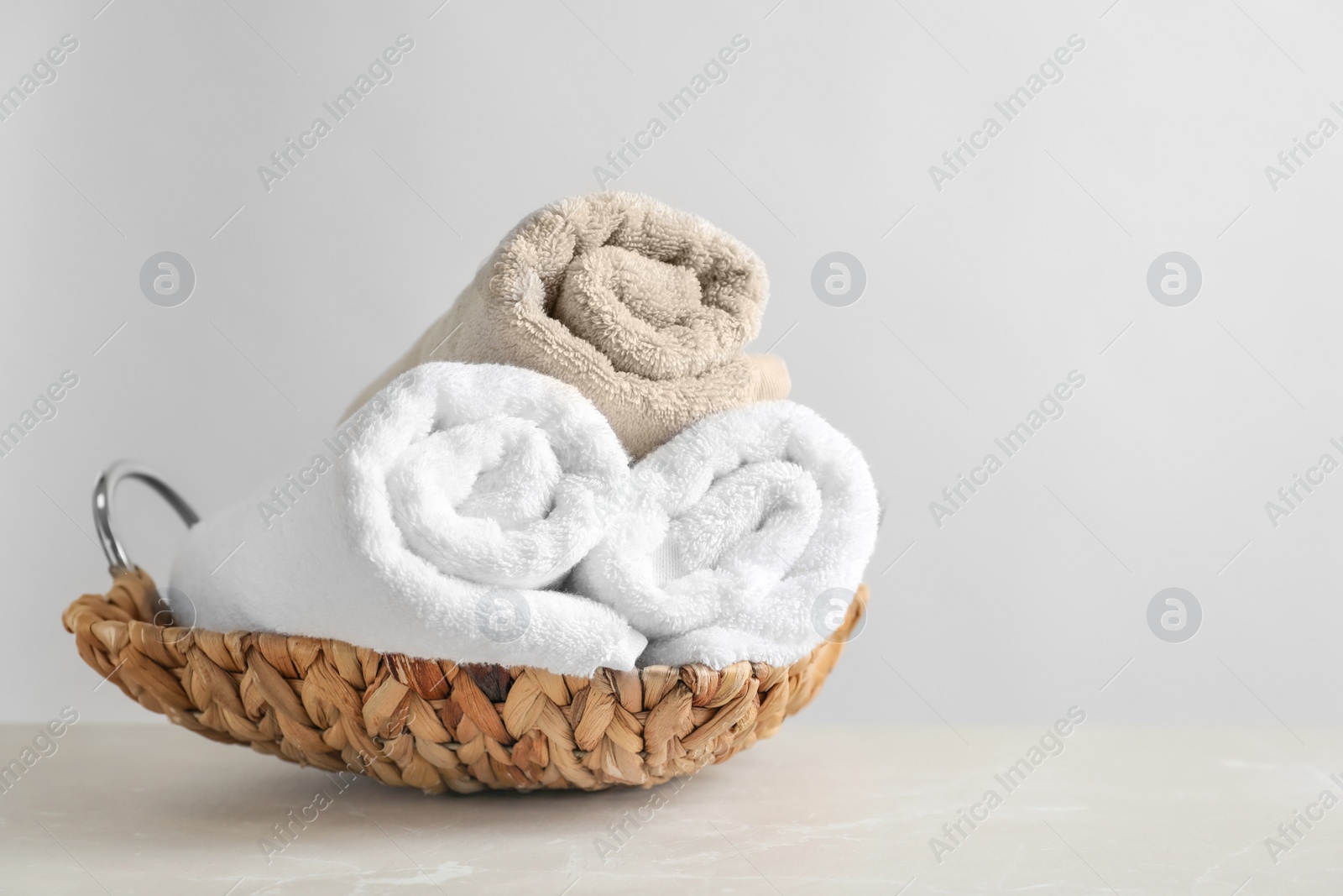 Photo of Basket with clean towels on table against light background