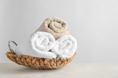 Photo of Basket with clean towels on table against light background