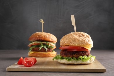 Photo of Board with delicious vegetarian burgers on grey table