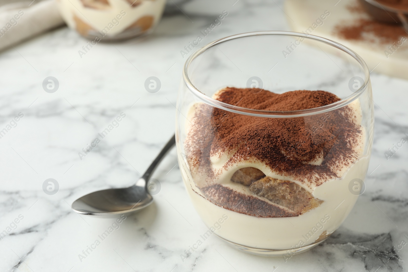 Photo of Delicious tiramisu in glass and spoon on white marble table, closeup. Space for text