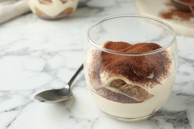 Delicious tiramisu in glass and spoon on white marble table, closeup. Space for text