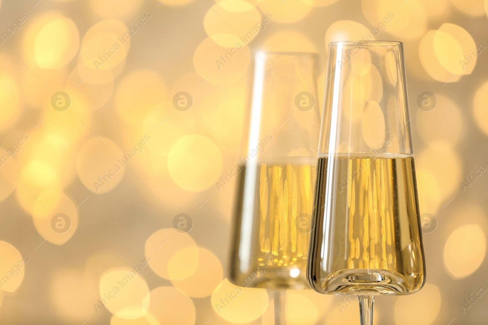 Photo of Glasses of fizzy champagne against blurred fairy lights, space for text