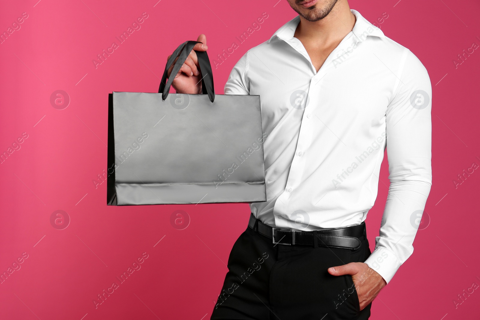 Photo of Young man holding black paper bag on pink background, closeup. Mockup for design