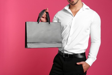 Photo of Young man holding black paper bag on pink background, closeup. Mockup for design