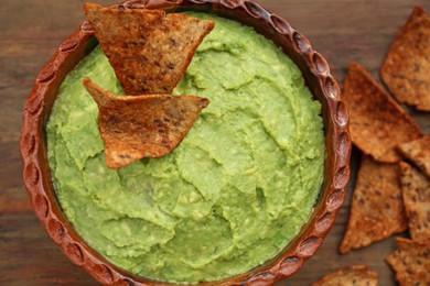Delicious guacamole made of avocados and nachos on wooden table, flat lay